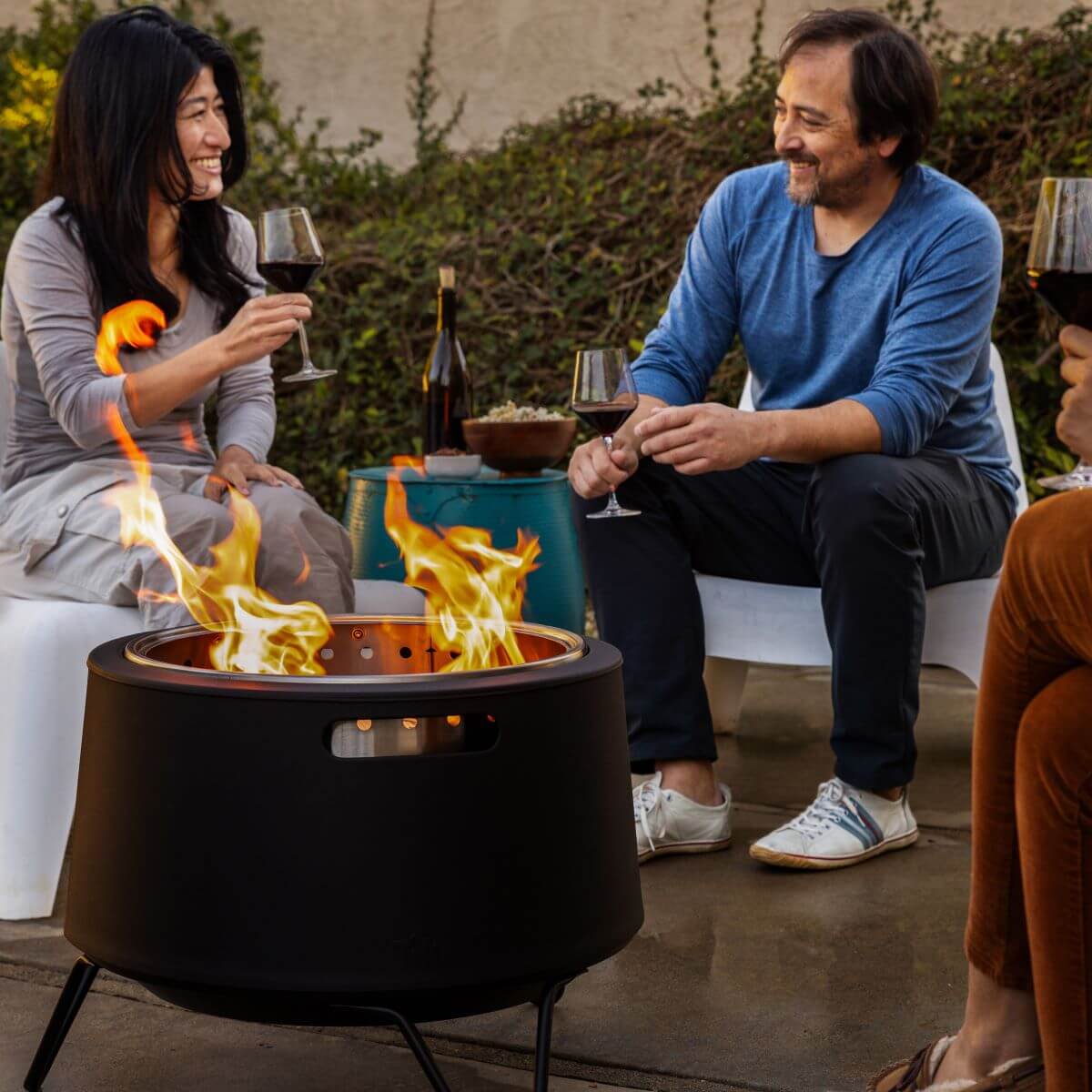 People enjoy wine and conversation around a TIKI® fire pit in a cozy outdoor patio setting.