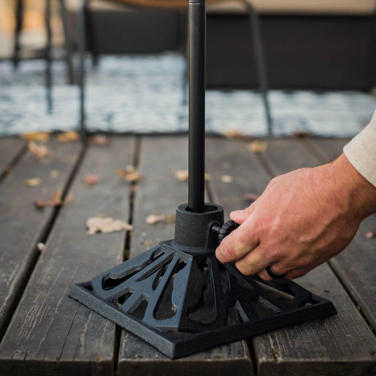 Hand securing a TIKI torch pole into a decorative black metal base on a wooden deck.