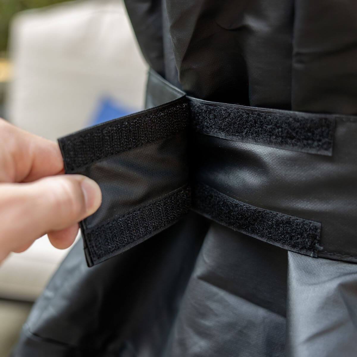 Close-up of a hand fastening the Velcro strap on a black TIKI fire pit cover for secure outdoor protection.