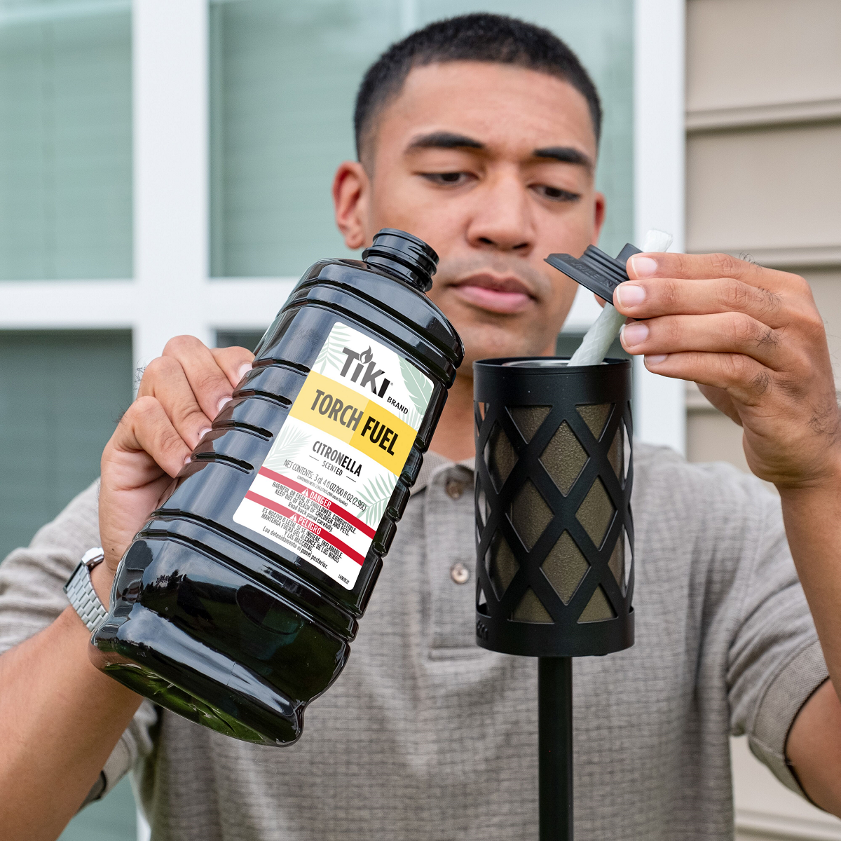 Person pouring TIKI Brand Citronella Torch Fuel into a black outdoor torch for backyard mosquito protection.