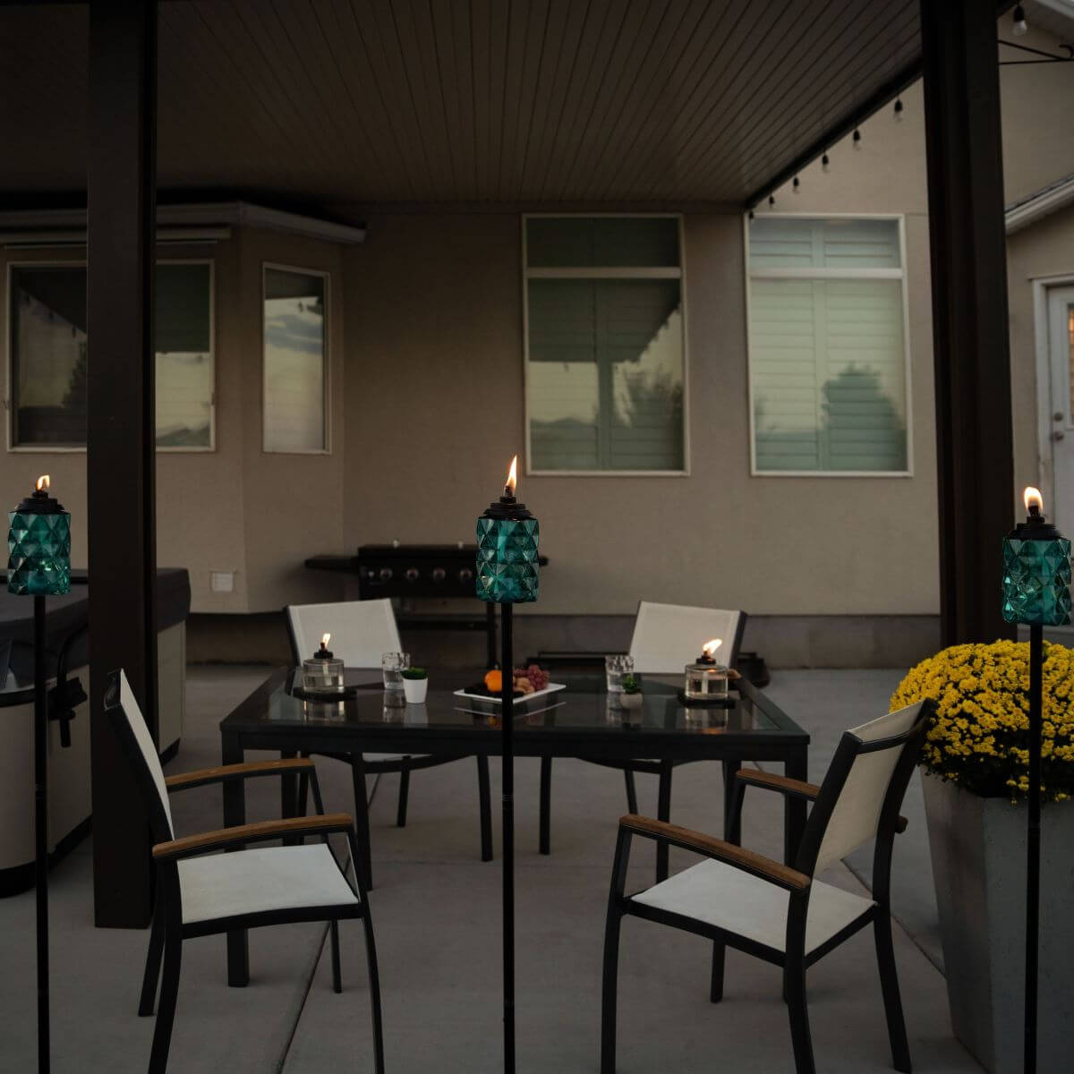 Accessible patio scene with lit TIKI® torches, outdoor table, chairs, and yellow flowers, ideal for evening gatherings.