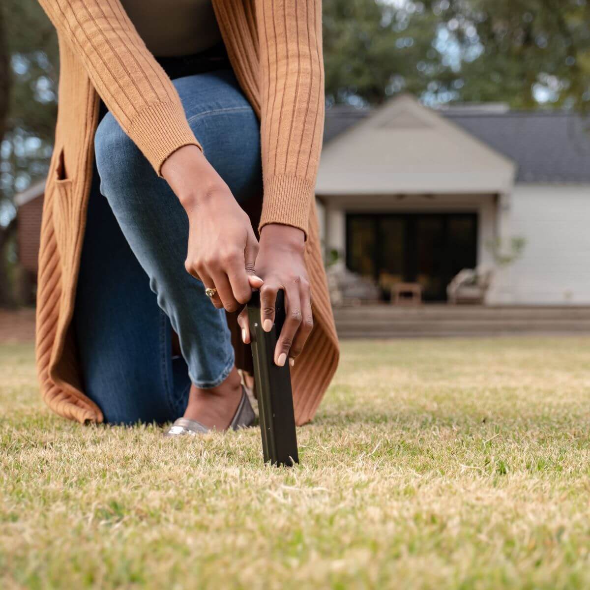 Person installing a TIKI® torch stake into the lawn in front of a house, preparing for outdoor use.