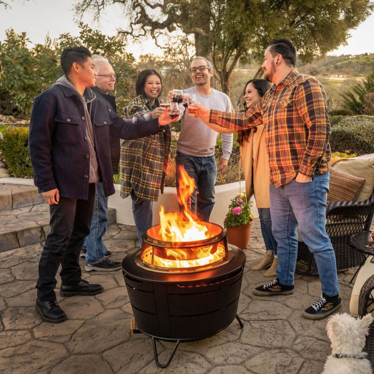 Group enjoying drinks around a TIKI® fire pit on a patio, creating a warm and inviting outdoor gathering atmosphere.