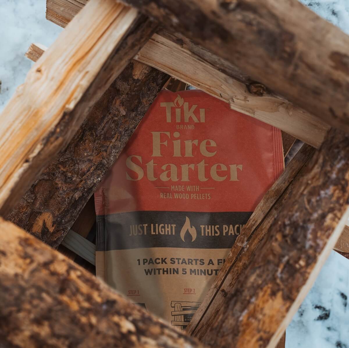 TIKI Brand Fire Starter pack placed under stacked firewood, ready to light for easy outdoor fire starting.