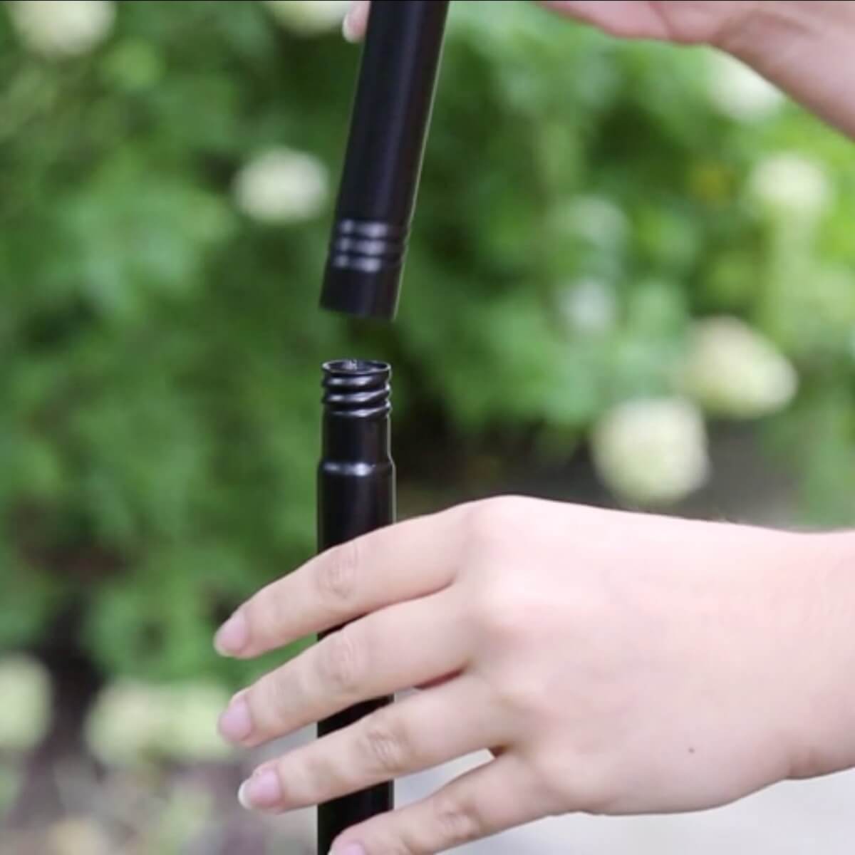 Hands assembling two black TIKI torch poles outdoors, showing easy screw-together connection for setup.