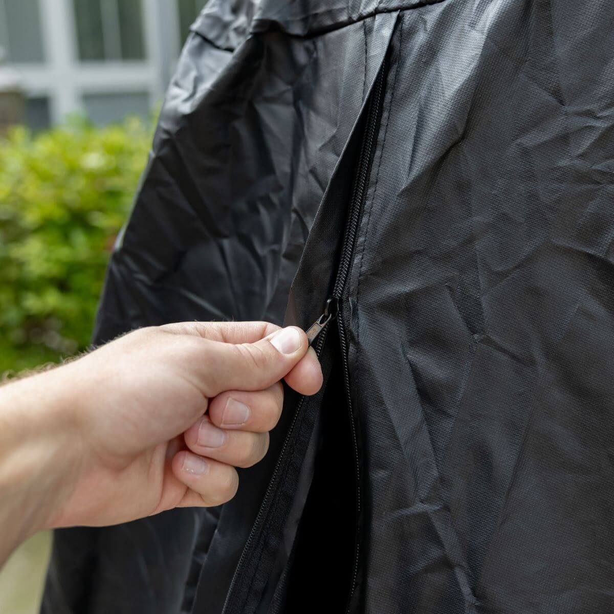 Hand unzipping a black outdoor fire pit cover; easy-access zipper for TIKI® fire pit protection.