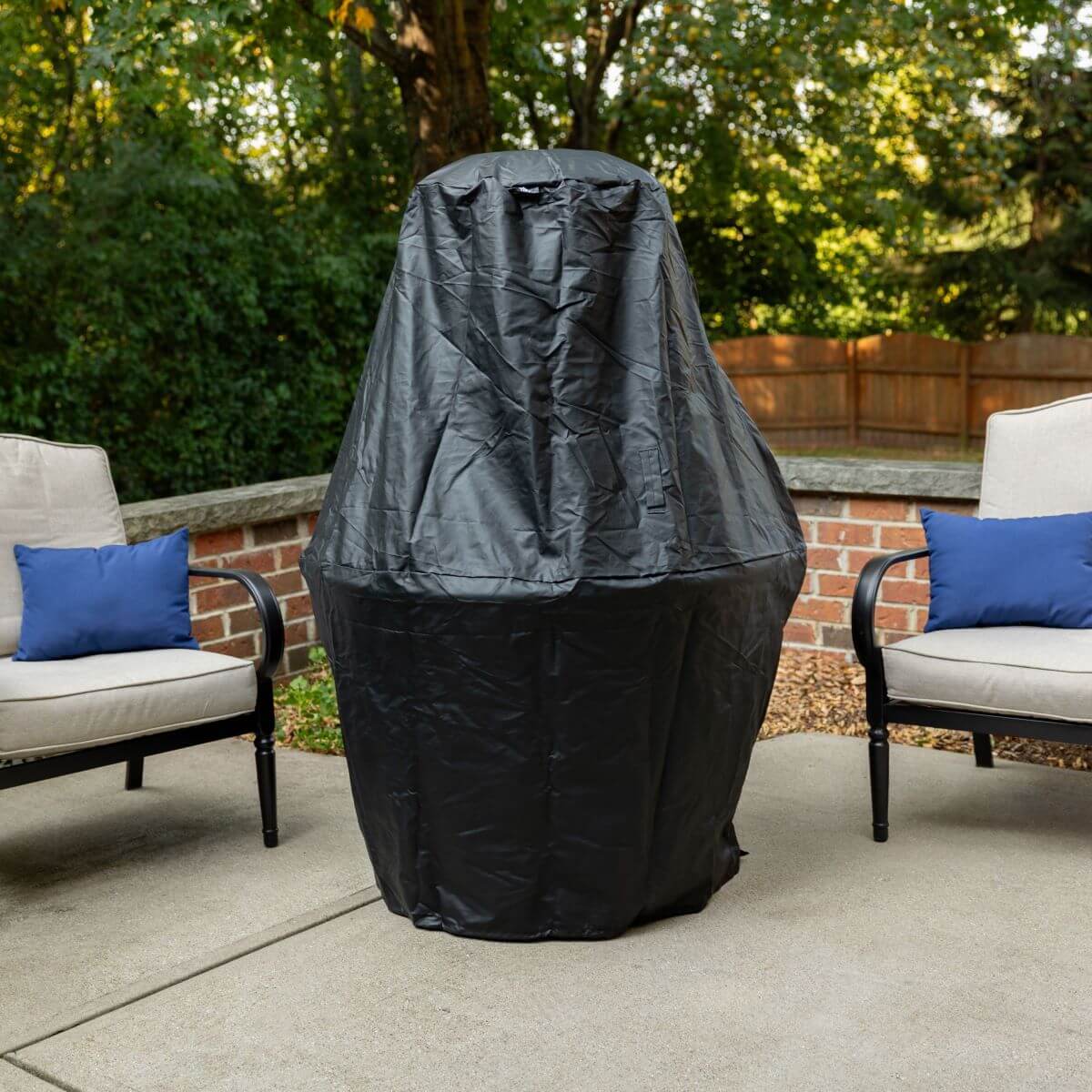 A TIKI fire pit covered with a black protective cover on a patio, surrounded by outdoor chairs with blue pillows.
