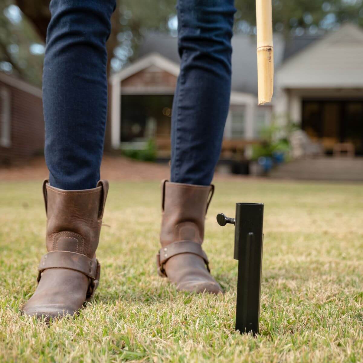 Person in boots installing a TIKI torch stake into grass in a backyard, preparing to set up an outdoor torch.