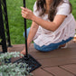 Woman securing a TIKI torch pole into a decorative metal base on a wooden deck, outdoors.