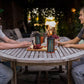 Two people enjoy snacks outdoors at a wooden table with TIKI® Brand lanterns, creating a cozy, inviting atmosphere.