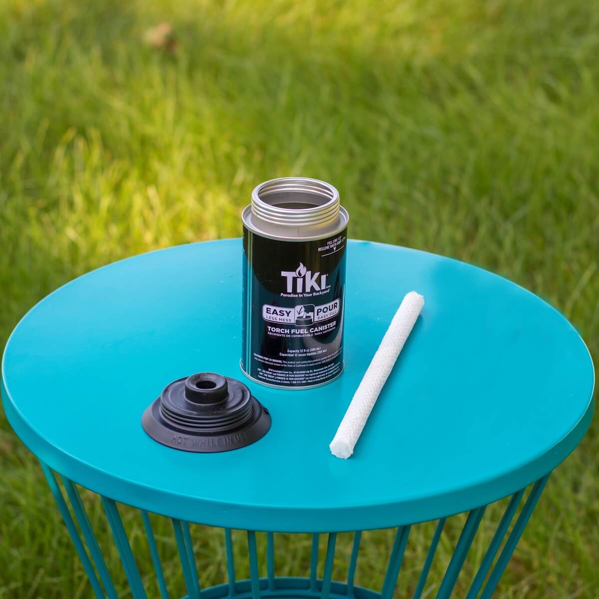 TIKI torch fuel canister, wick, and cap on a teal table outdoors, ready for assembly.