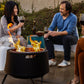 People enjoy wine and conversation around a TIKI® fire pit in a cozy outdoor patio setting.