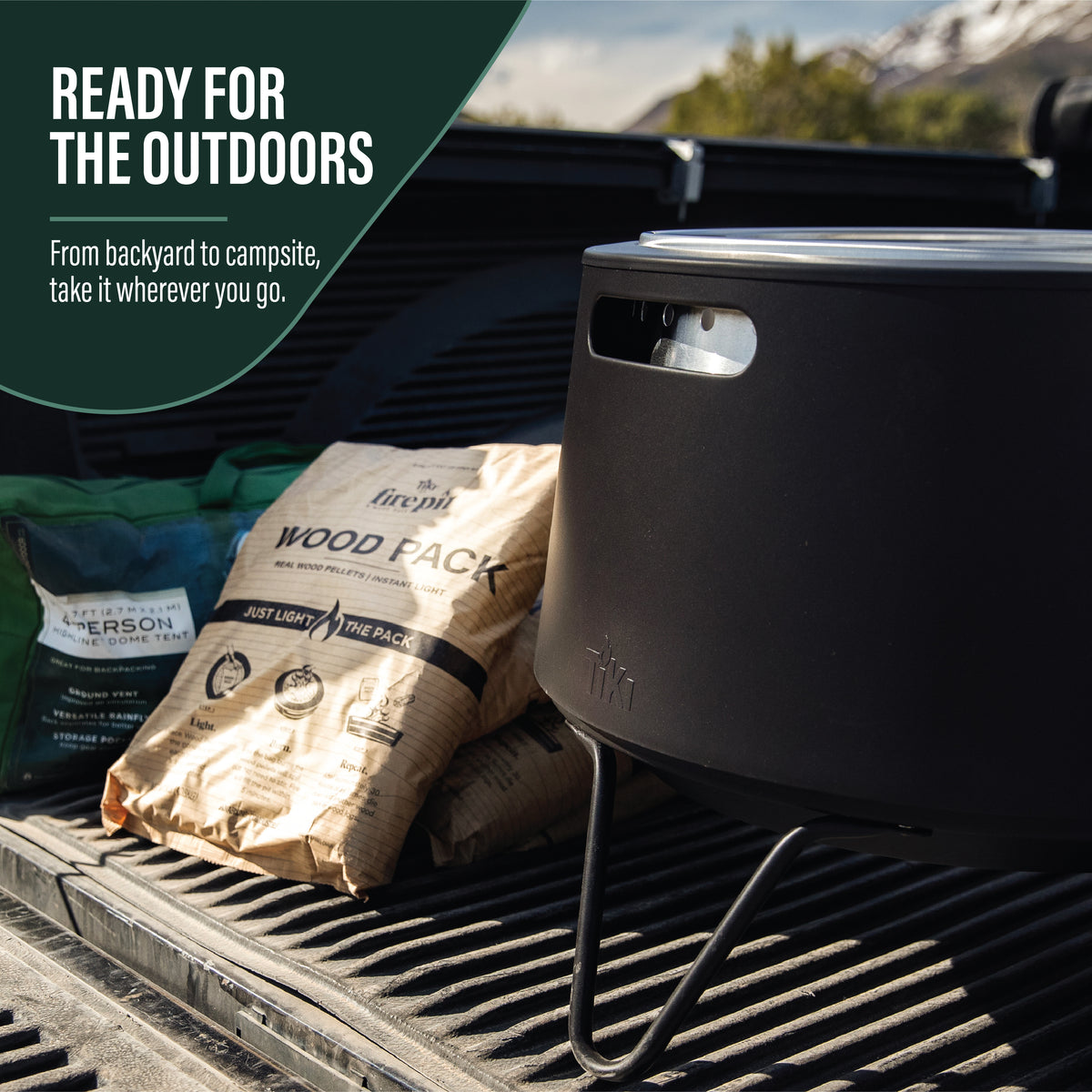 Portable black fire pit with wood pack, set on a truck bed, ideal for outdoor use. Easy to carry and set up anywhere.
