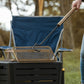 Person using a long-handled tool to lift a mesh spark screen from a TIKI fire pit outdoors.