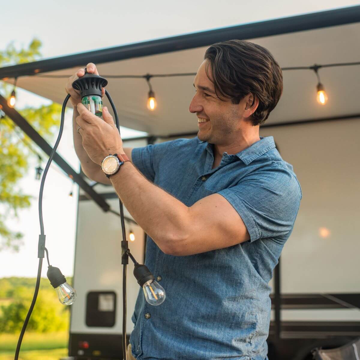 Person installs TIKI BiteFighter LED string lights outdoors near an RV, enhancing ambiance and mosquito protection.