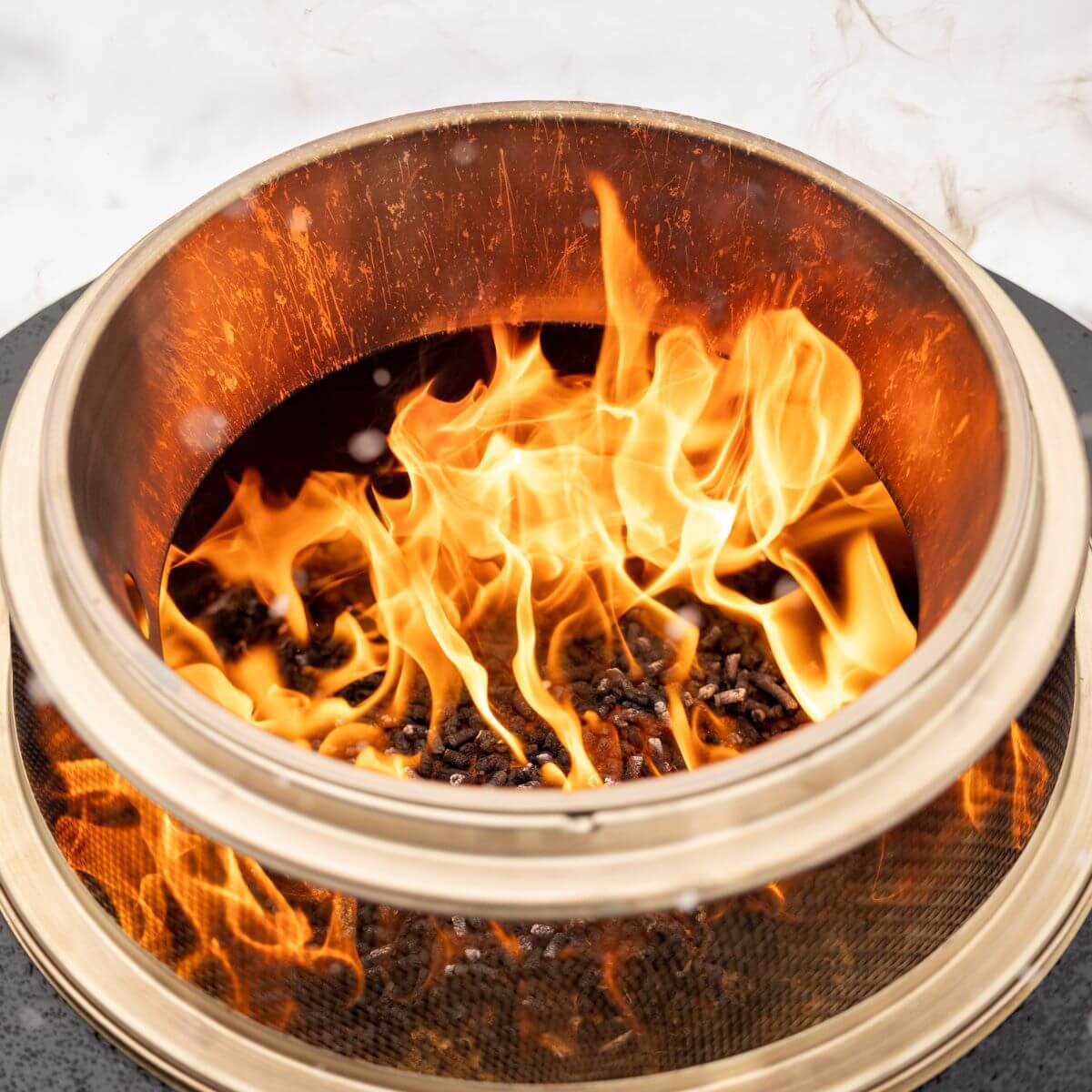 Close-up of a TIKI® fire pit with bright flames and wood pellets burning inside a stainless steel bowl.