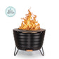 Round black metal fire pit with visible flames, sturdy legs, and a modern design. "The Spruce Approved" badge shown.