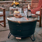 Black round fire pit table with glass top, lanterns, and snacks.
