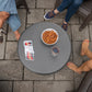 Round gray table with UNO cards, a bowl of pretzels, and a glass of red drink, surrounded by three people’s legs.