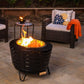 Black TIKI fire pit with bright flames on a patio, surrounded by wicker chairs and a side table with drinks.