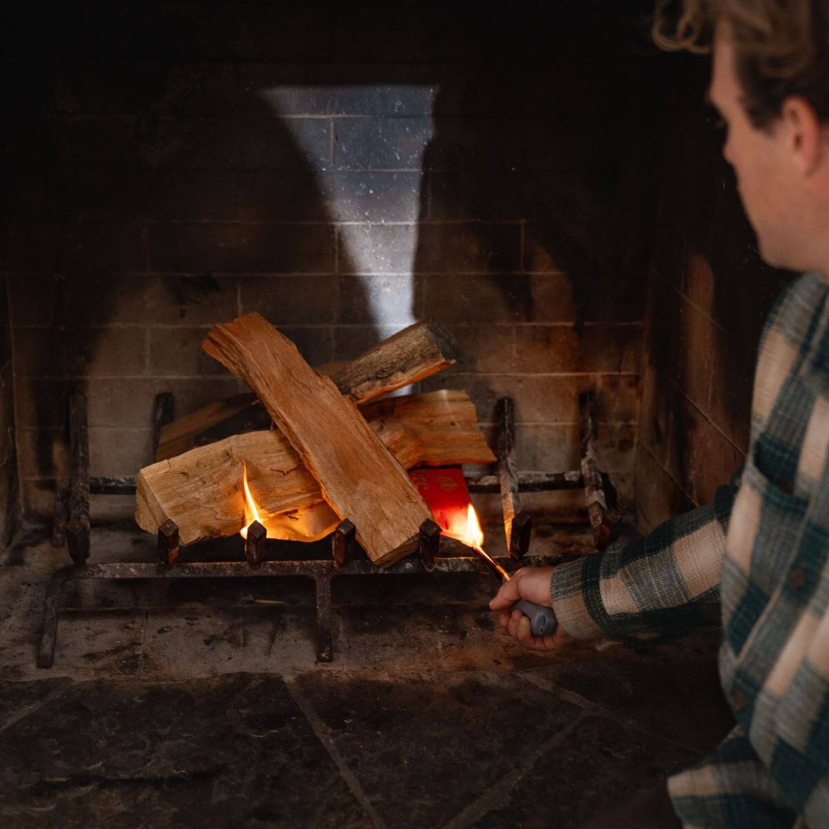 Person lighting a wood-burning indoor fireplace with a fire starter, creating a cozy and warm atmosphere.