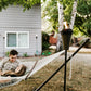 A TIKI® torch glows beside a hammock in a cozy backyard, creating a relaxing outdoor ambiance near a home.