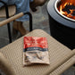 Red Tiki Fire Starter pack on wicker chair near fire pit.