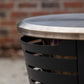Close-up of a TIKI® fire pit rim and black metal slatted side, with a brick wall in the background.