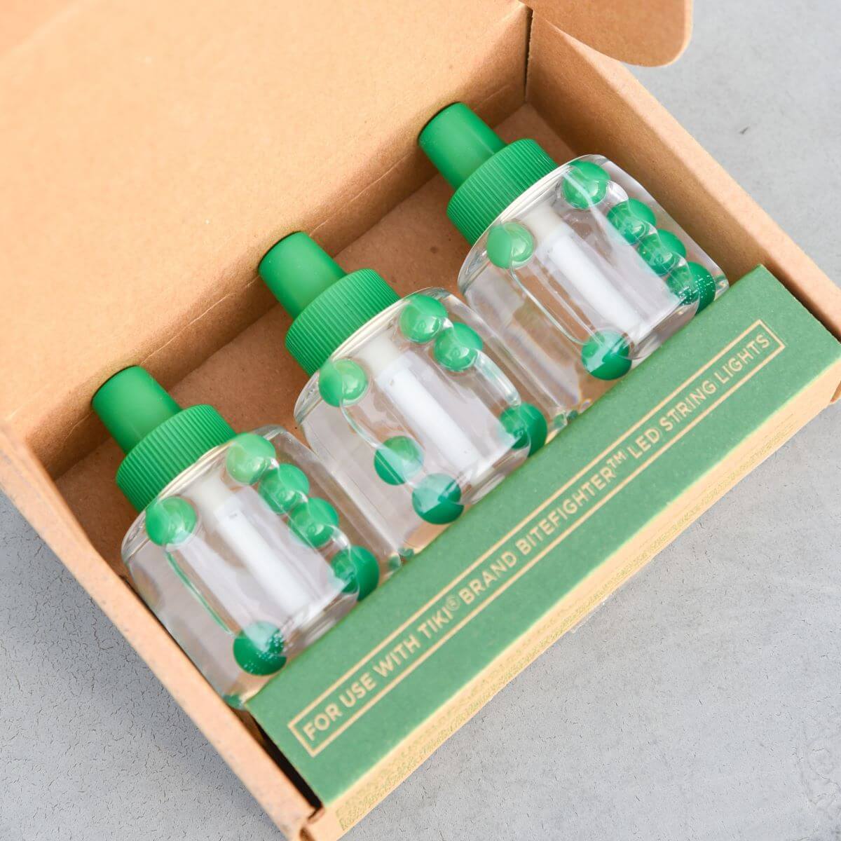 Three TIKI Brand BiteFighter LED string light repellent refill bottles in an open cardboard box.