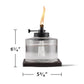 Clear glass TIKI® tabletop torch with flame, 6.25" tall and 5.75" wide, shown on a dark wood base.