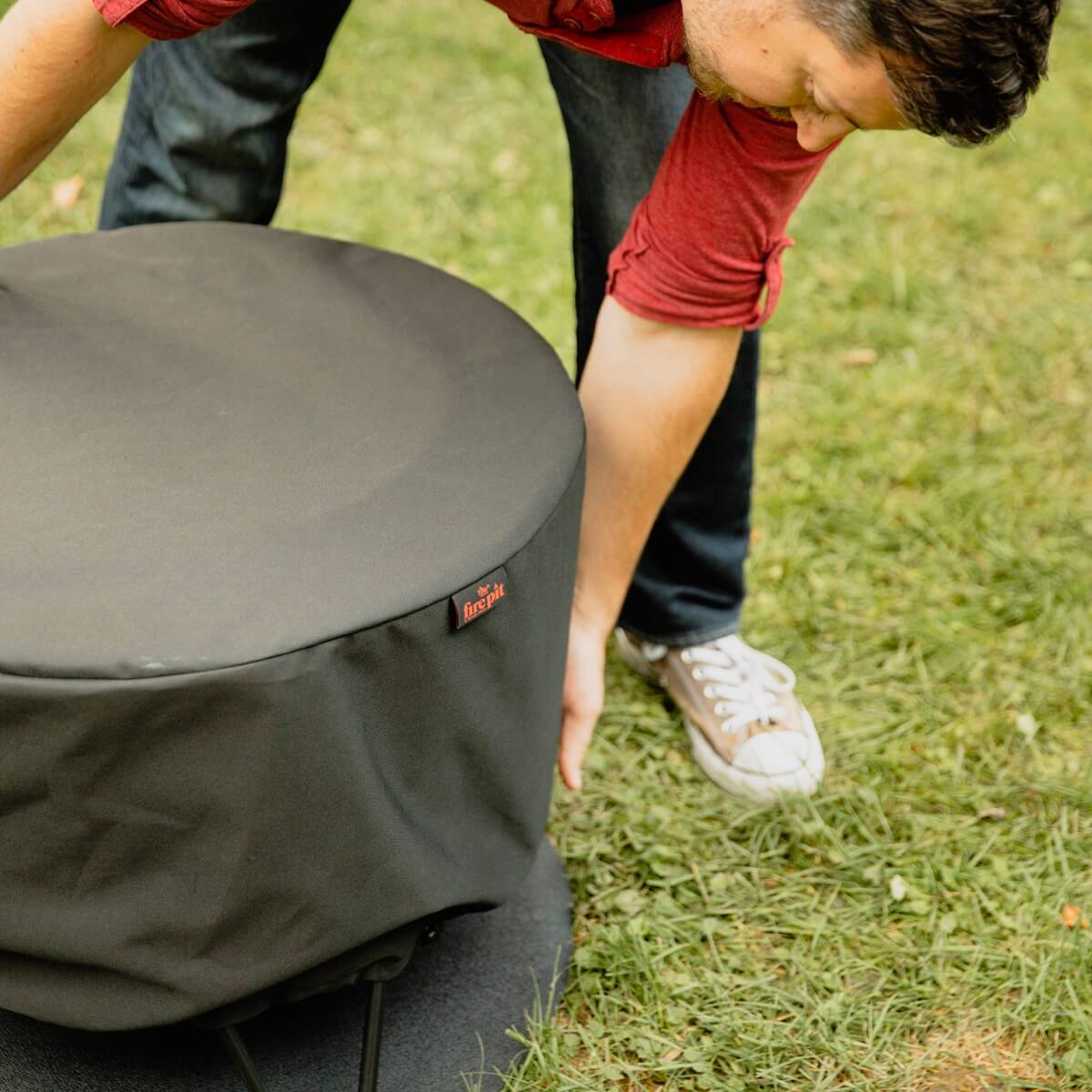 TIKI Brand Patio Smokeless Fire Pit Replacement Cover, person placing cover on fire pit outdoors