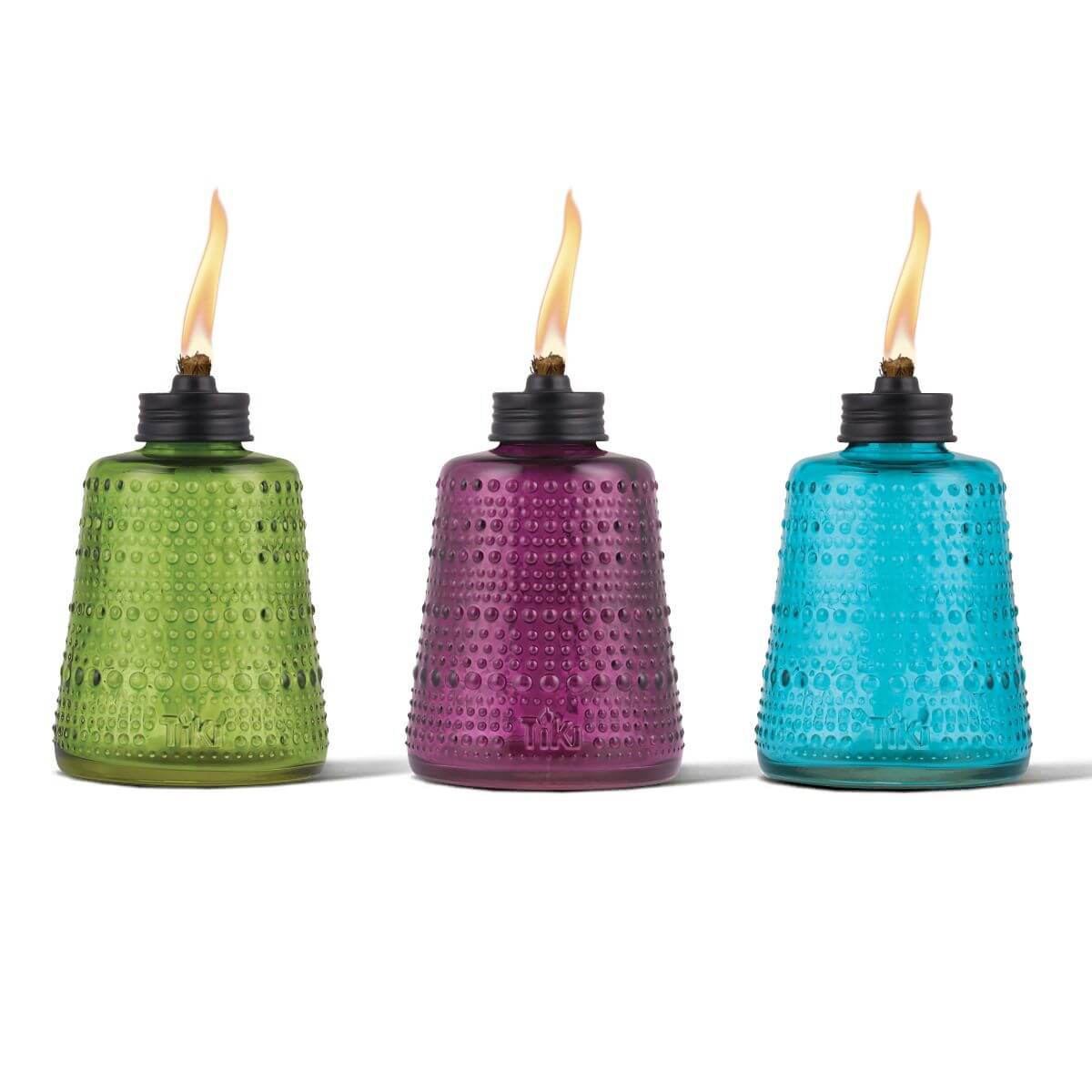 Three textured glass TIKI® table torches in green, purple, and blue, each lit with a visible flame.