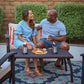 Couple enjoying snacks and drinks outdoors with TIKI Brand lanterns on a patio table, creating a cozy, inviting atmosphere.