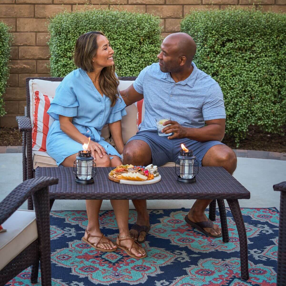 Couple enjoying snacks and drinks outdoors with TIKI Brand lanterns on a patio table, creating a cozy, inviting atmosphere.