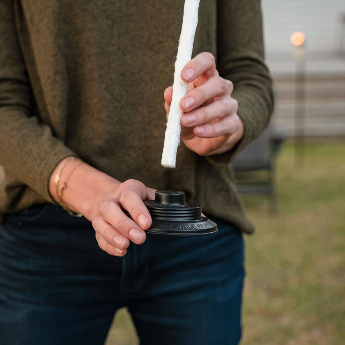 Person inserting a replacement wick into a TIKI Brand torch cap outdoors.