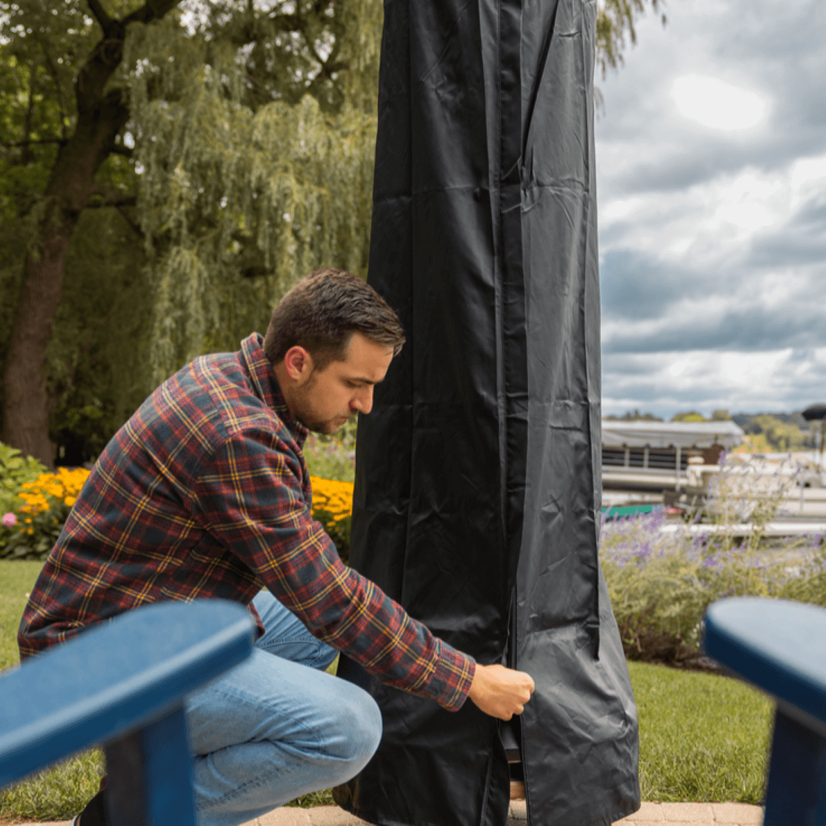 Person zipping up a black outdoor cover on a TIKI Brand patio torch in a garden setting.