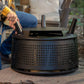 Person attaches a handle to a black TIKI Brand fire pit, which is upside down on an outdoor rug.
