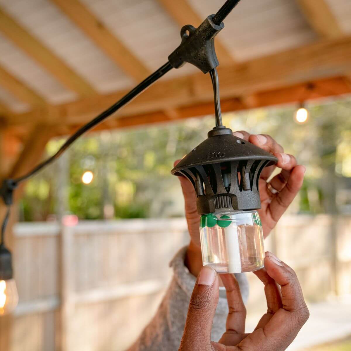 Person installs a TIKI mosquito repellent device on an outdoor string light under a covered patio.