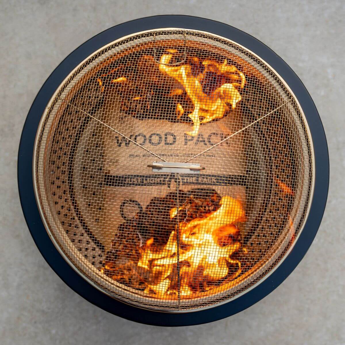 Black fire pit with mesh cover, burning wood inside.