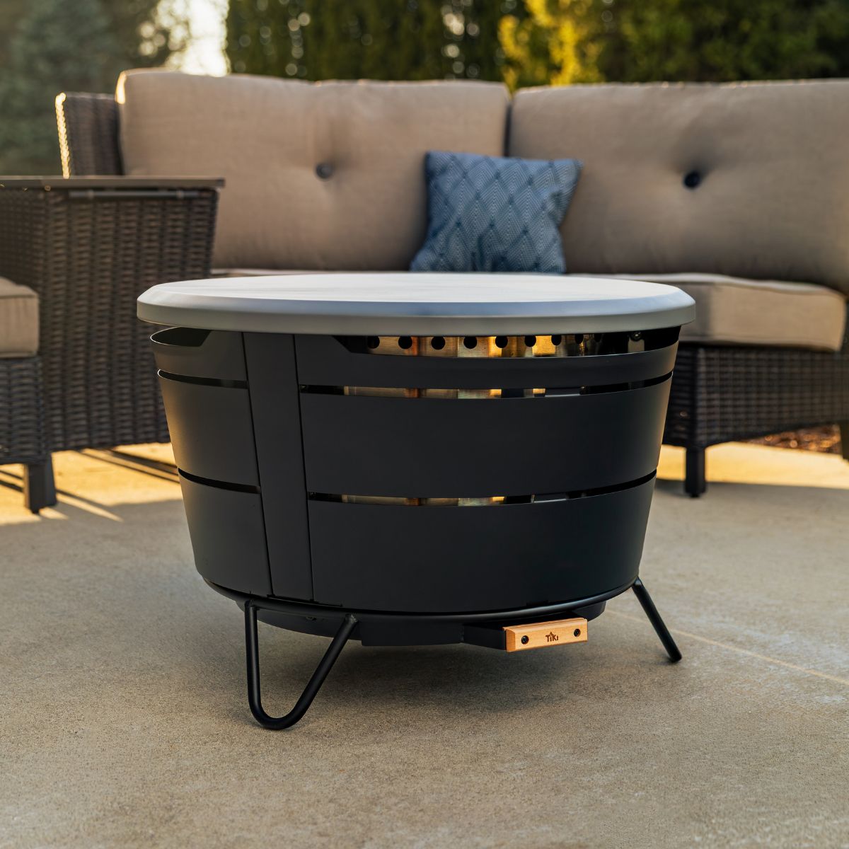 TIKI Brand Reunion Tabletop Cover in gray on fire pit, outdoor patio setting with sofa in background
