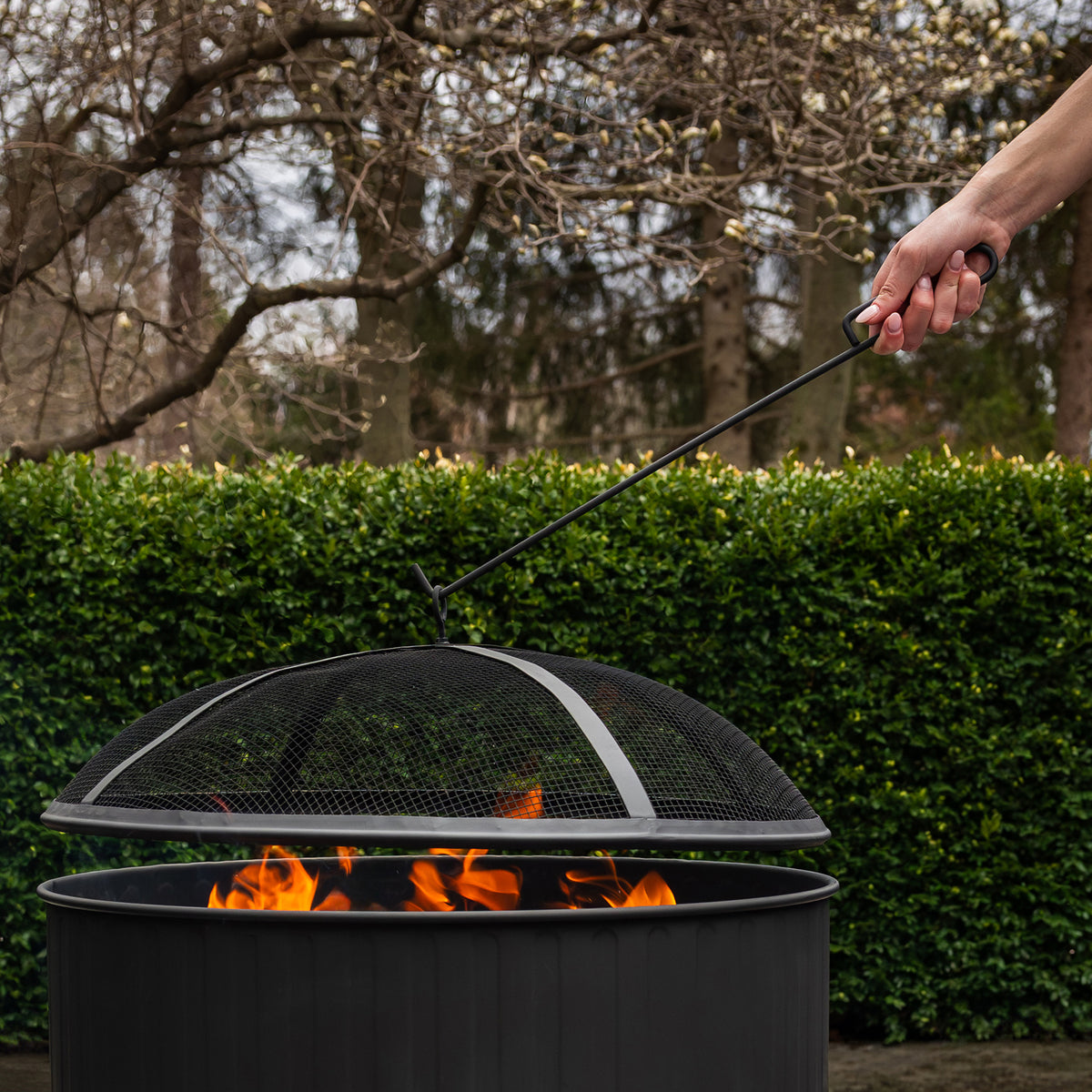 Black fire pit with mesh lid and handle, flames visible inside.