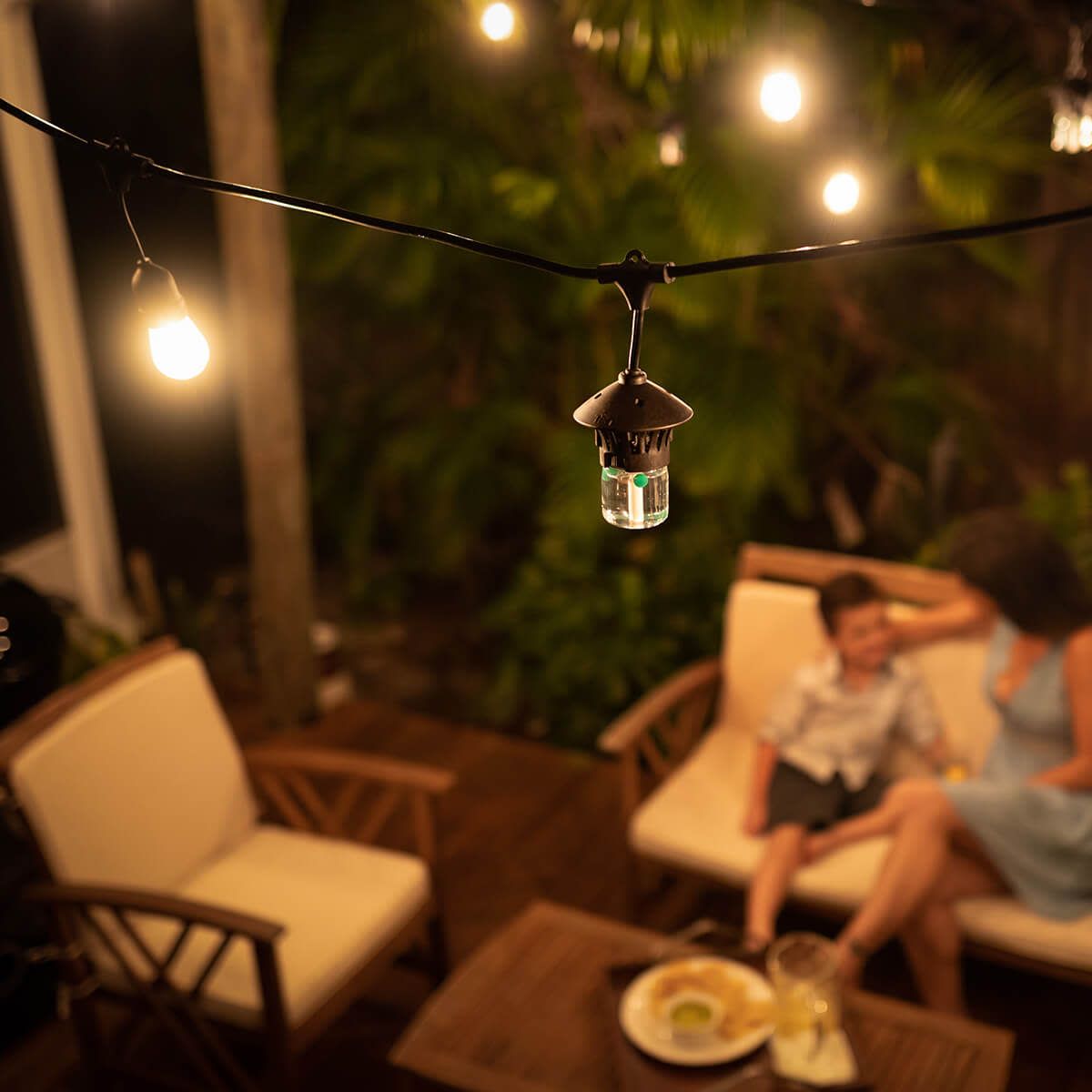 Outdoor patio with string lights and a TIKI mosquito repellent device, cozy seating, and a table with food and drinks.