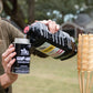 Person pours TIKI Brand torch fuel into an easy-pour canister outdoors, next to a bamboo torch.