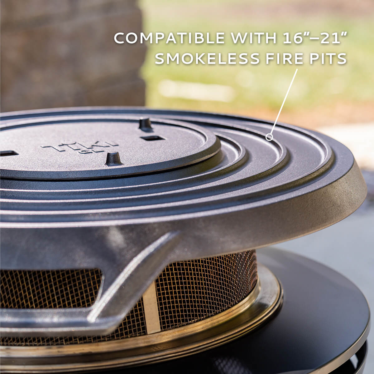 Close-up of a TIKI fire pit accessory lid, compatible with 16–21 inch smokeless fire pits, outdoors.