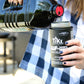 Person pouring TIKI Brand torch fuel into a black canister, wearing a blue plaid shirt.