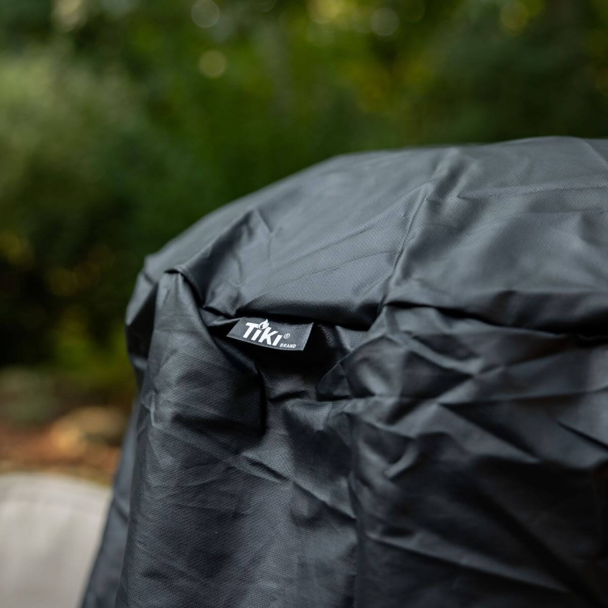 Close-up of a black TIKI Brand fire pit cover outdoors, showing the TIKI logo tag for easy identification.