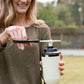 Woman trimming the wick of a TIKI Brand outdoor torch with scissors in a backyard setting.