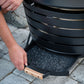 A person pulls out the ash pan from a TIKI fire pit for easy cleaning on a stone patio.