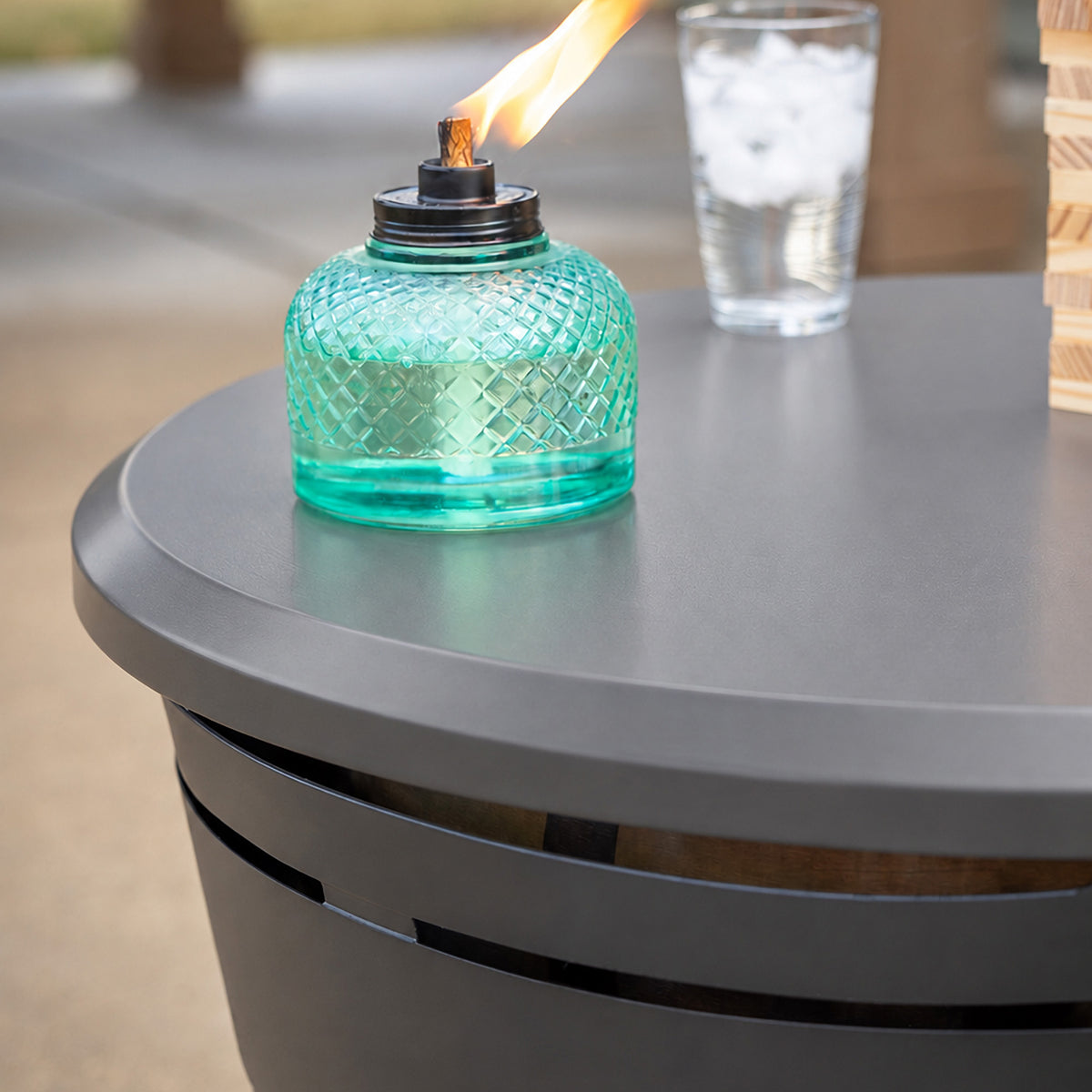 TIKI Brand Reunion Tabletop Cover gray, close-up view installed on fire pit with torch and drink on top