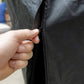 Close-up of a hand zipping a black outdoor cover, designed to protect TIKI fire pits from weather.